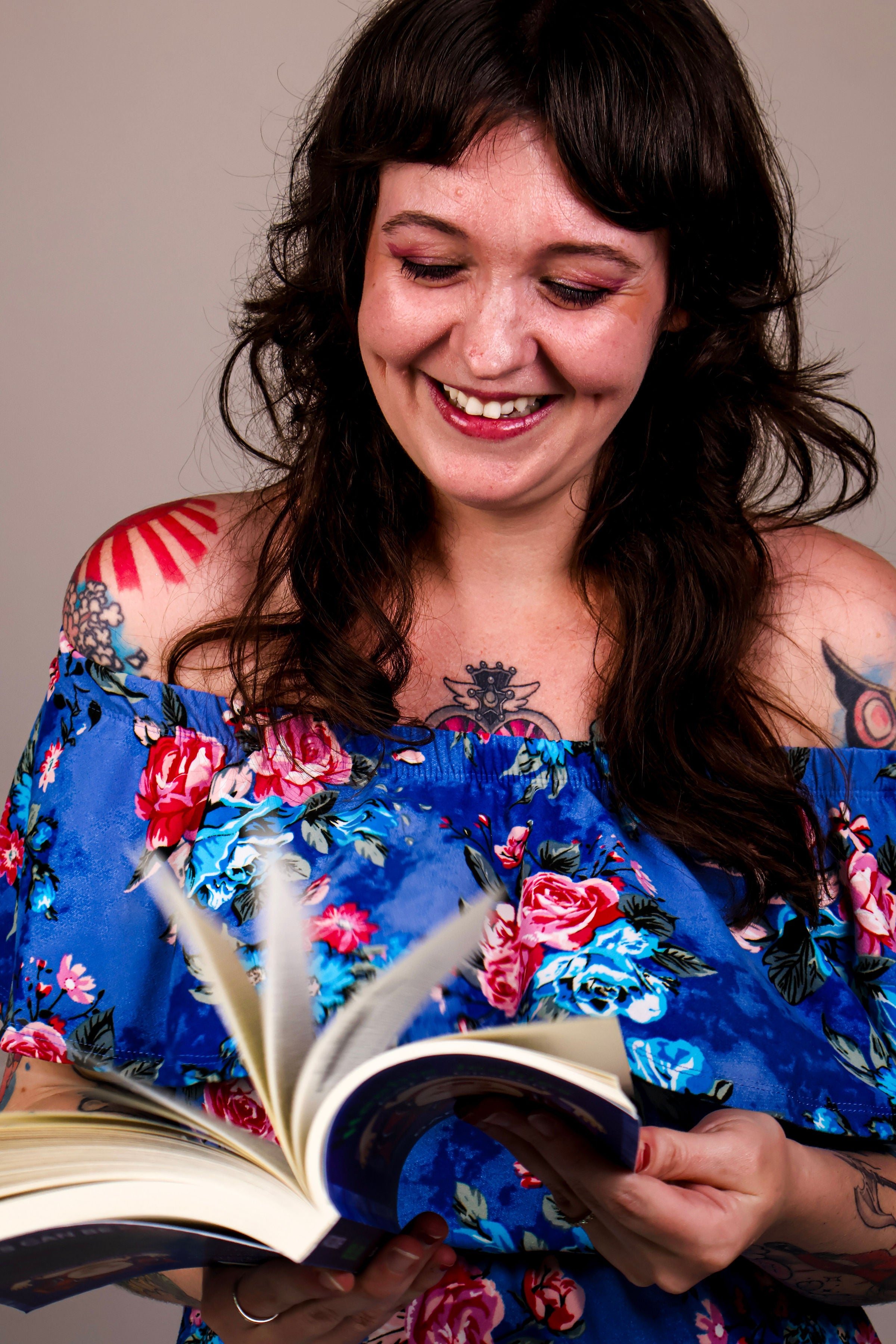 Woman in a blue floral dress holding an open book, smiling.