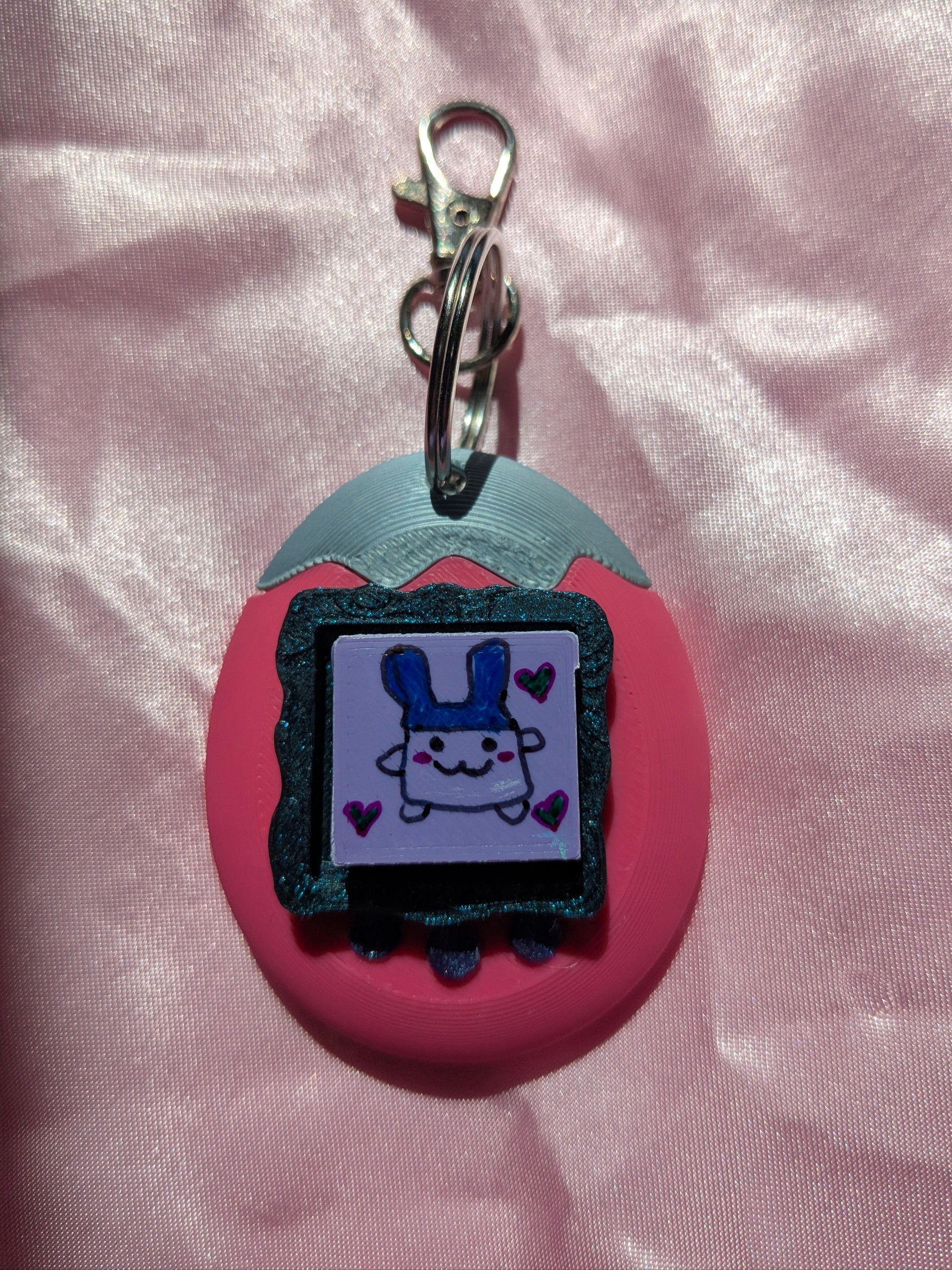 Keychain with cartoon character design on a pink fabric background.