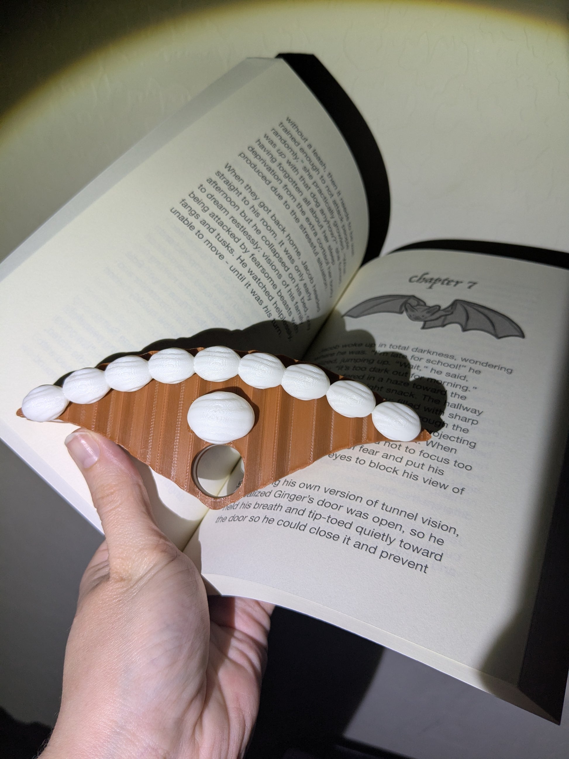 Hand holding a plastic book holder that looks like a cake on an open book